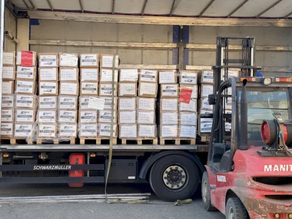 Voll beladene Lkw-Pritsche mit Paletten voller Offroad- und SUV-Teile, daneben ein Gabelstapler