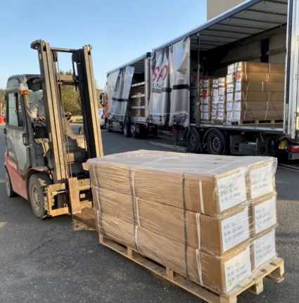 Gabelstapler transportiert eine folierte Palette mit SUV- und Offroad-Teilen vor dem Lkw