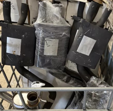 Schwarze Auspuff-Schalldämpfer mit Endrohren in einer Gitterbox im Lager