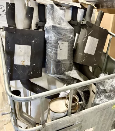 Auspuffanlagen und polierte Edelstahl-Endrohre in einer Gitterbox, teils foliert