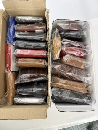 Zwei Kartons mit dicht gepackten Echtleder-Geldbörsen in Blau, Rot, Cognac, Braun und Schwarz, jeweils in Schutzfolie.