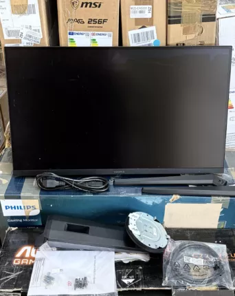 Ausgepackter PC-Monitor mit Netzkabel, Standfuß und Montagezubehör vor mehreren Monitor-Kartons
