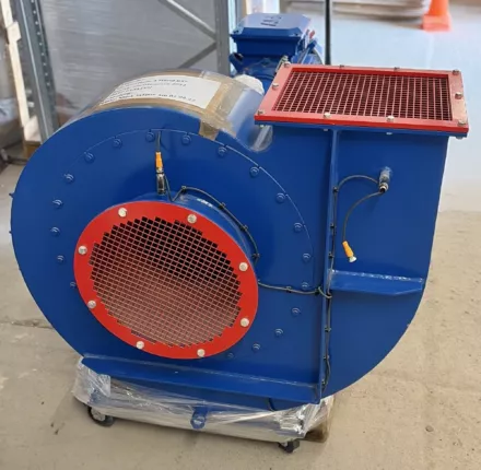 Zentrifugalventilator mit spiralförmigem Gehäuse und rotem Schutzgitter am Ansaug – Dreiviertelansicht auf Palette