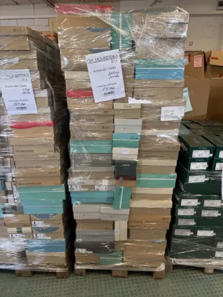 Hohe Palettenstapel mit türkis-beigen Marken-Schuhkartons und Warenposten-Etiketten im Lager